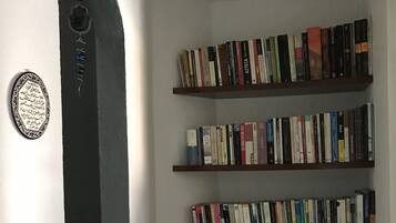 A bookshelf with multiple shelves filled with books, a decorative mirror, and a small wall-mounted object.
