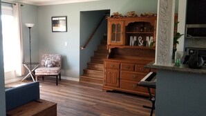 Un salón con una escalera de madera, un sillón estampado y un aparador con adornos.