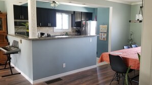 Una cocina moderna con armarios oscuros, un refrigerador de acero inoxidable y una ventana. Hay un comedor con una mesa cubierta con un mantel rojo y sillas negras.