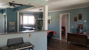 Una sala de estar con ventilador de techo, un piano, un comedor con mesa y sillas, y un pasillo que conduce a otra habitación.
