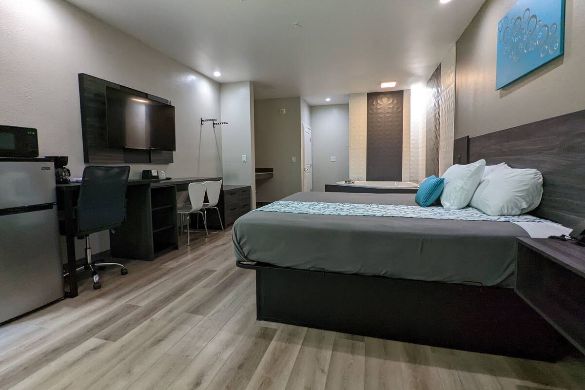 A modern hotel room with a bed, desk, chair, and a flat-screen TV.
