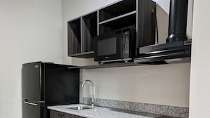 A modern kitchen with dark wood cabinets, a black refrigerator, a stainless steel sink, and a microwave. - Crystal Inn Jacinto City (Houston)