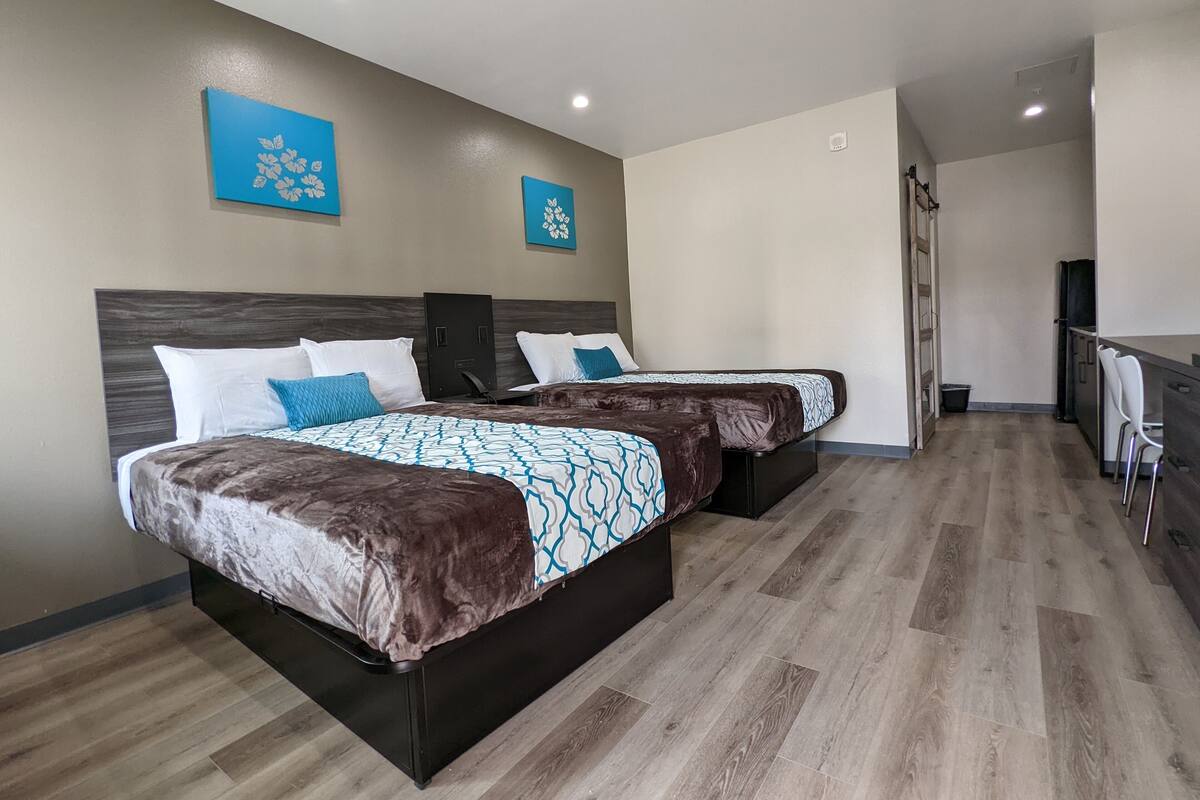 A hotel room with two beds, a kitchenette, and a bathroom.