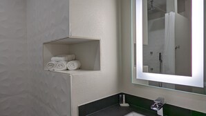 A bathroom with a white sink, a glass shelf with towels, a mirror, and a shower area. - Crystal Inn Jacinto City (Houston)