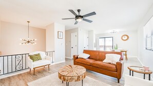 A modern living room with a white sofa, a brown leather couch, a wooden coffee table, a ceiling fan, and a chandelier. - Cozy 2BD Near Hospital (Wichita)