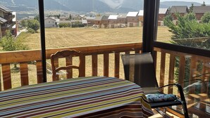 Une pièce avec une table et des chaises, de grandes fenêtres donnant sur un paysage rural avec des montagnes.
