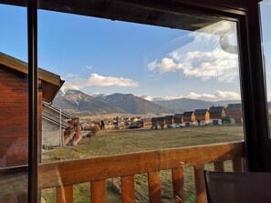Une vue depuis une fenêtre donnant sur une zone rurale, avec des bâtiments en bois et des montagnes en arrière-plan.