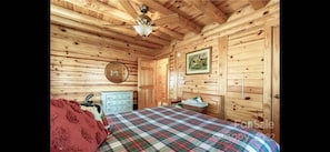 A wooden cabin bedroom with a plaid bedspread, a ceiling fan, a dresser, and a framed picture on the wall.