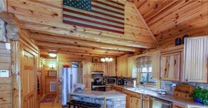 A wooden cabin interior with a kitchen featuring a stone island, wooden cabinets, and a large American flag.