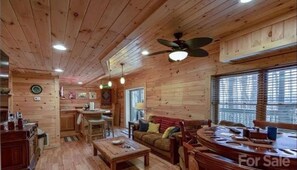 A wooden cabin interior with a dining area, kitchen, and living room.