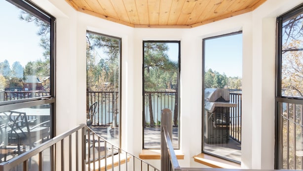 Ein modernes Interieur mit großen Fenstern, Holzboden und Blick auf einen See und Bäume.