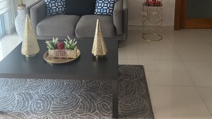 Una sala de estar con un sofá gris, una mesa de centro negra, una obra de arte enmarcada sobre el sofá, una planta en maceta y una pequeña mesita con vasos rojos.