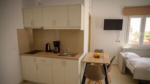 Een ruimtelijk kitchenette met een koffiezetapparaat, een spoelbak en kasten. Er is een eethoek met een tafel en stoelen, en een bed met een raam.