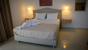 Een net opgemaakt bed met witte lakens en twee handdoeken in de vorm van zwanen, een schilderij van een zonsondergang boven de oceaan aan de muur, en twee bedlampjes.