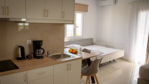 Een compacte kitchenette met een koffiezetapparaat, spoelbak en een klein eethoekje met een stoel.