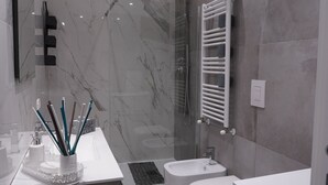 A modern bathroom with a marble wall, a white sink, a toilet, and a shower area. - Puglia in love (Margherita di Savoia)