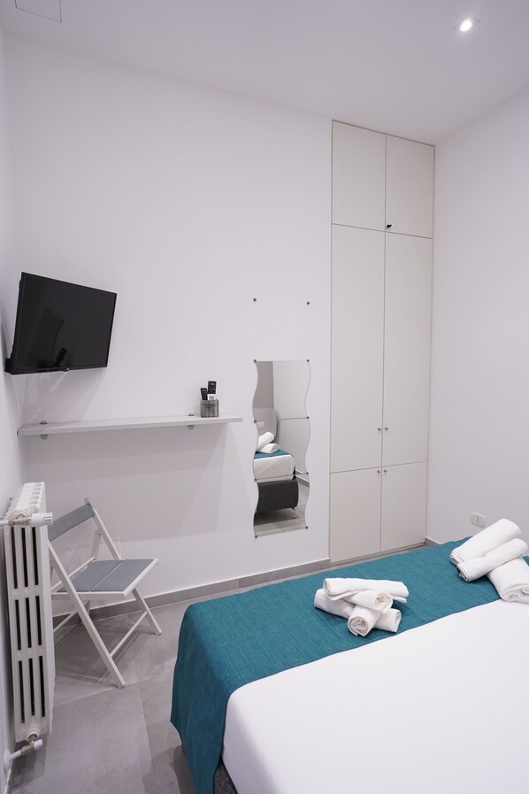 A hotel room with a bed, a TV mounted on the wall, a wardrobe, and a radiator.
