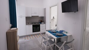 A compact kitchen with white cabinets, a gas stove, and a small dining area with a table and chairs. - Puglia in love (Margherita di Savoia)