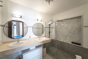 Une salle de bain moderne avec deux lavabos, un grand miroir, une douche et un espace douche fermé par des parois de verre.