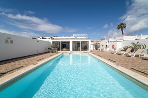En swimmingpool med krystalklart, blåt vand, et overdækket opholdsområde og en hvid bygning med et skilt.