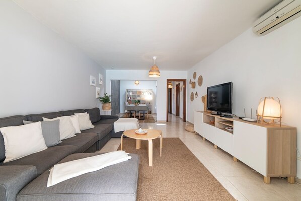 A modern living room with a grey sofa, a coffee table, a TV, and a white cabinet. - Stylish 2 bedroom and 2 bathroom Villa with private pool & roof terrace (Playa Blanca)