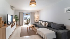 En moderne stue med sofa, fjernsyn og et spiseområde med bord og stole.