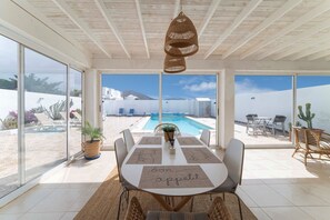Un coin repas avec vue sur la piscine, des chaises en osier et une table avec un set de table.