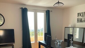 A dining area with a table, chairs, a TV, and a balcony with curtains. - T5 house overlooking Toulon harbour with swimming pool (Le Revest-les-Eaux)