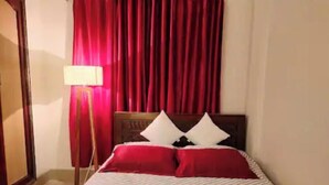 A hotel room with a bed, red curtains, a lamp, and a wooden headboard. - 3 Bedroom Apartment near Dhanmondi & Panthpath (Dhaka)