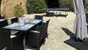 Un área de comedor al aire libre con mesas y sillas de mimbre, una mesa cubierta y una pérgola.