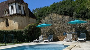 Una piscina con sillones de descanso y un muro de piedra.