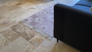 Una habitación con paredes de piedra, techo de madera, un banco acolchado, una alfombra estampada y un sofá oscuro.