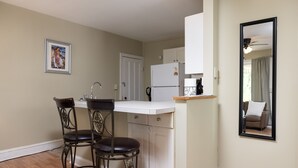 Une cuisine compacte avec un réfrigérateur blanc, un petit plan de travail et deux tabourets de bar.