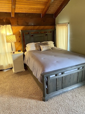 A bedroom with a wooden bed, a nightstand with a lamp, and a thermostat.