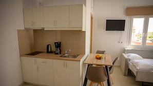 A compact kitchenette with a coffee maker, a sink, and cabinets. There is a dining area with a table and chairs, and a bed with a window. - Sunsea studios close to the beach- Mountain view studio 6 (Κάτω Γούβες)