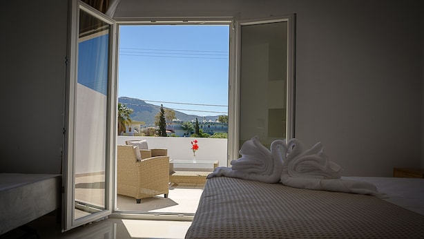 A hotel room with a bed, a wicker chair, and a view of the outside. - Sunsea studios close to the beach- Mountain view studio 6 (Κάτω Γούβες)