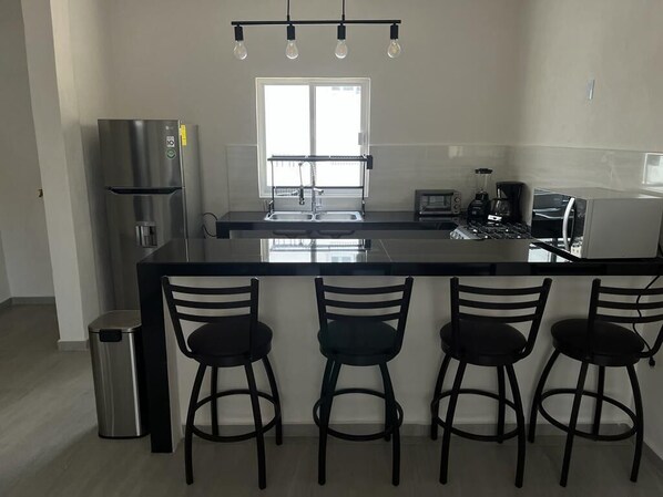 Una cocina moderna con una isla central, electrodomésticos de acero inoxidable y taburetes de bar.