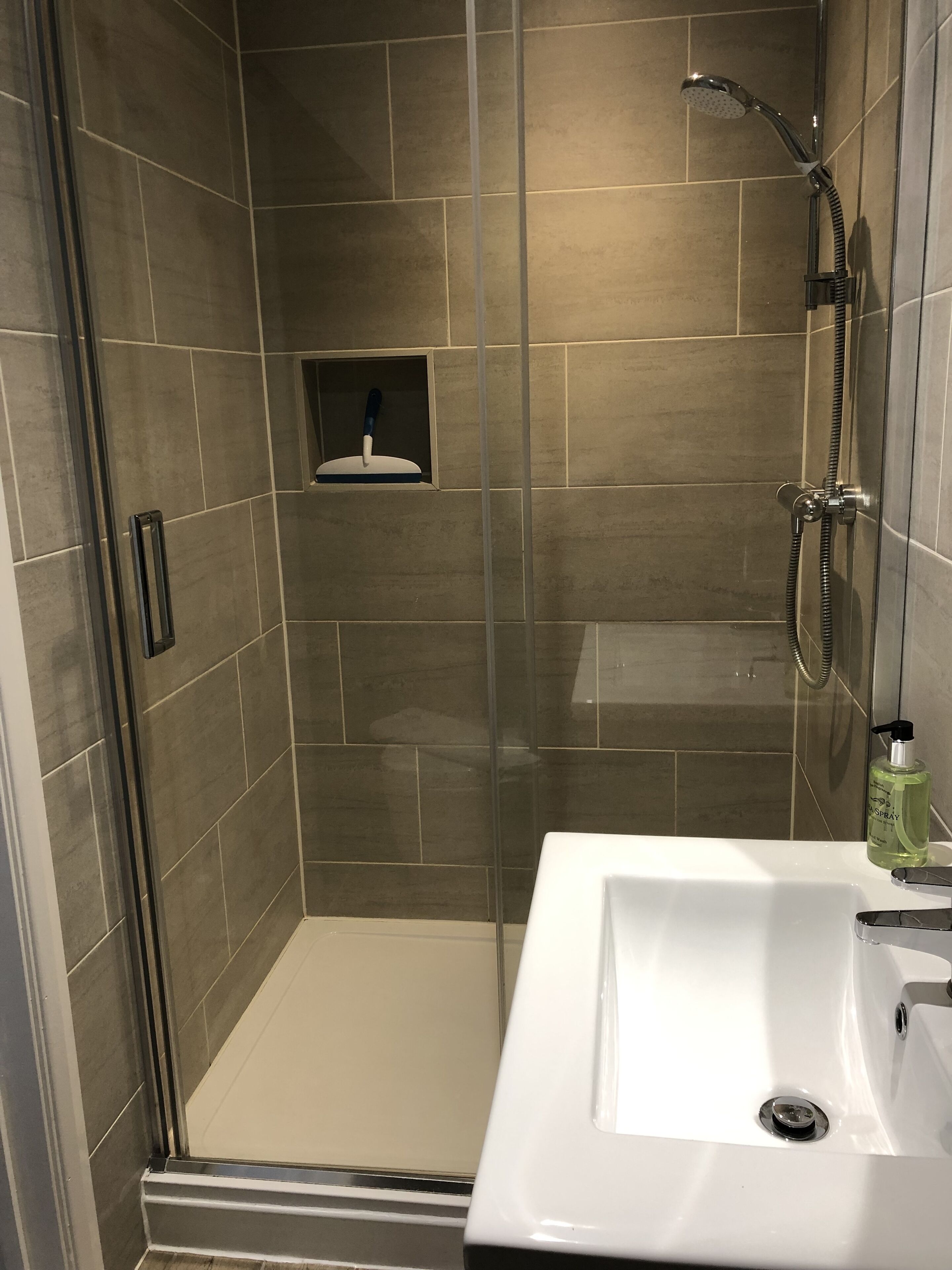A shower with a handheld showerhead and a handheld scrubber.