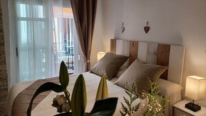 Ein Hotelzimmer mit Bett, Nachttisch, Lampe und Blick auf den Außenbalkon durch transparente Vorhänge.