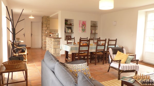 A dining area with a table set for four, surrounded by wooden chairs. A sofa with patterned cushions is in the foreground.