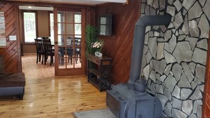 A cozy living room with a stone wall, wooden flooring, a fireplace, and a dining area with chairs and a table.
