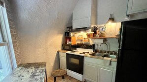 A compact kitchen with white cabinets, a black stove, and a sink. There are two stools and a wooden table.