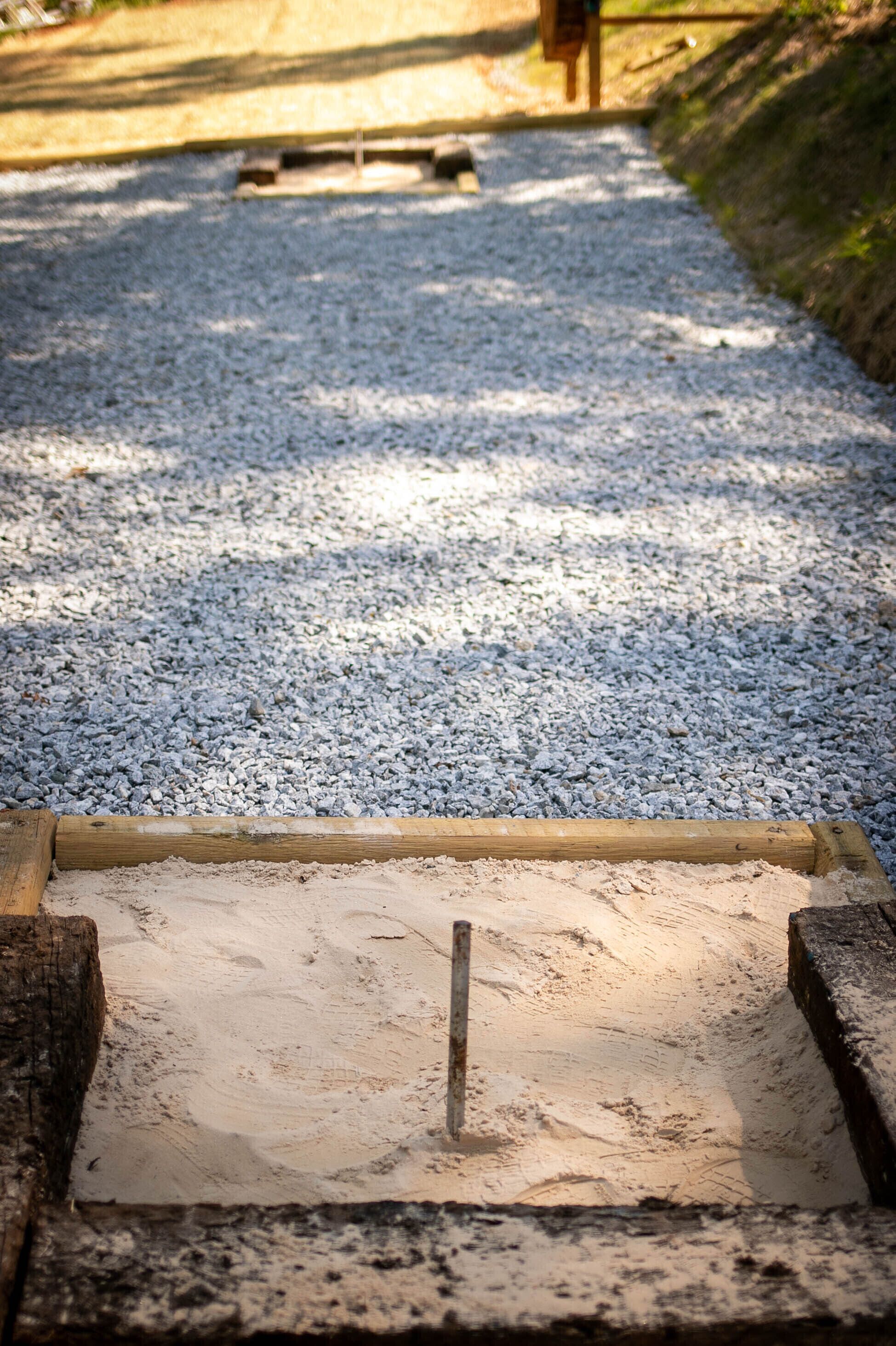 A gravel path with a wooden board and a metal pole in the foreground.