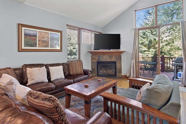 A living room with a brown leather sofa, a wooden coffee table, a fireplace, and a television mounted above it. - Beautiful Home with Private Hot Tub Deck Fireplace (Breckenridge)