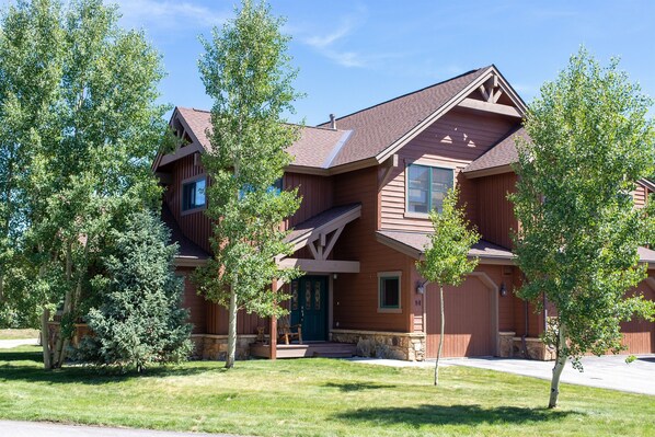 A two-story wooden house with a green door, a front porch, and a stone foundation.