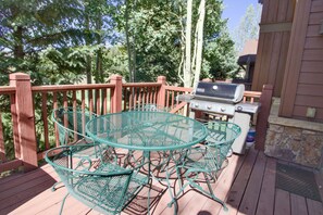 A wooden deck with a metal table and chairs, a barbecue grill, and a stone wall. - Beautiful Home with New Private Hot Tub. Fireplace (Breckenridge)