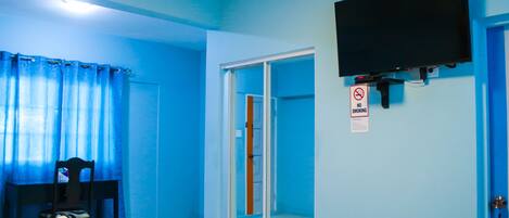 Una stanza con un letto, una sedia, una televisione fissata al muro e una porta scorrevole.