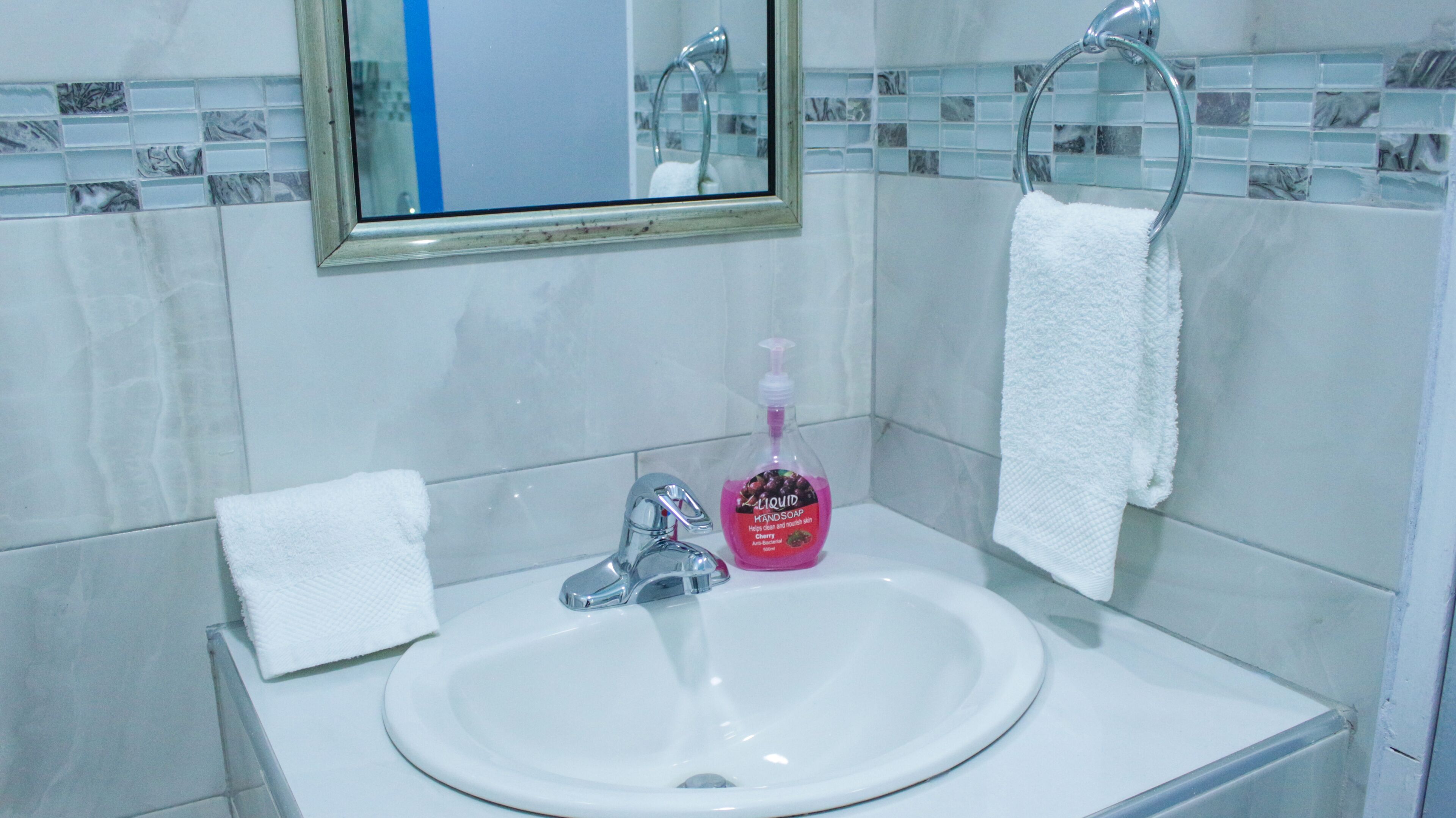 A bathroom with a white sink, a mirror, and a hand soap dispenser.