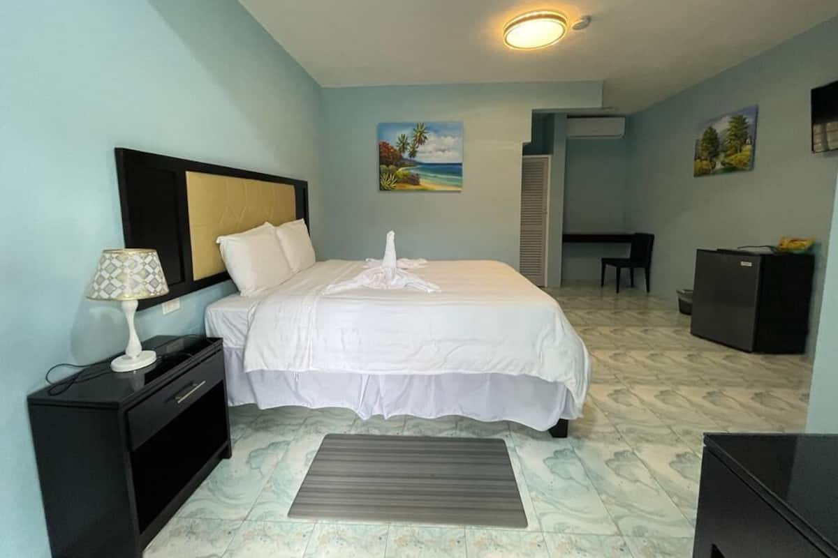 Ein Hotelzimmer mit Bett, Nachttisch, Lampe und einem kleinen Schreibtisch mit Computer.