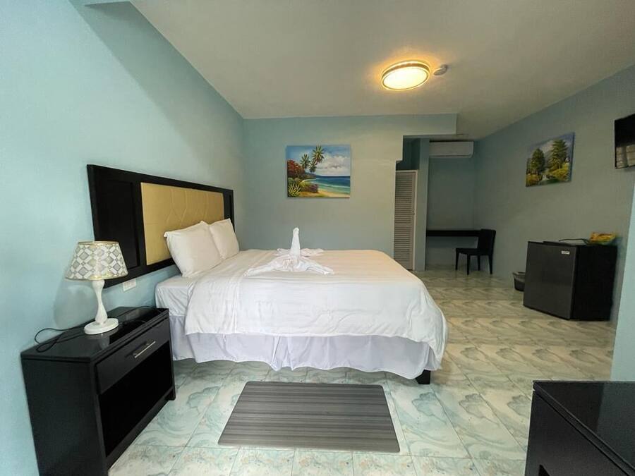A hotel room with a bed, nightstand, lamp, and a small desk with a computer.